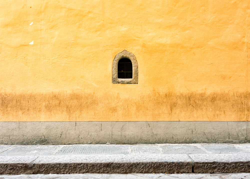 A small wine window within a yellow wall in Florence