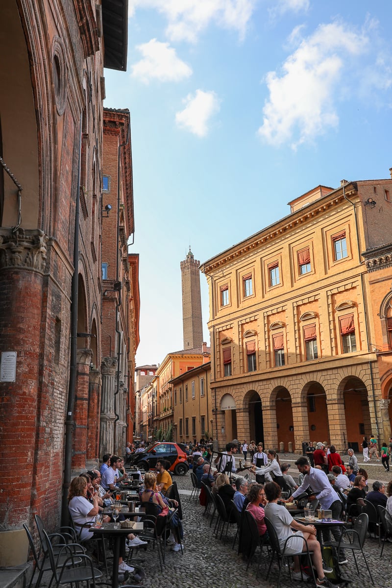 Lots of people sitting at restaurant tables outdoors in a piazza in Bologna, Italy