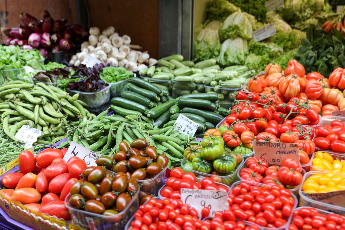 Vibrant and fresh vegetables, like tomatoes and zucchini, for sale at a market in Bologna - visiting the many food markets is one of the best things to do in Bologna! 