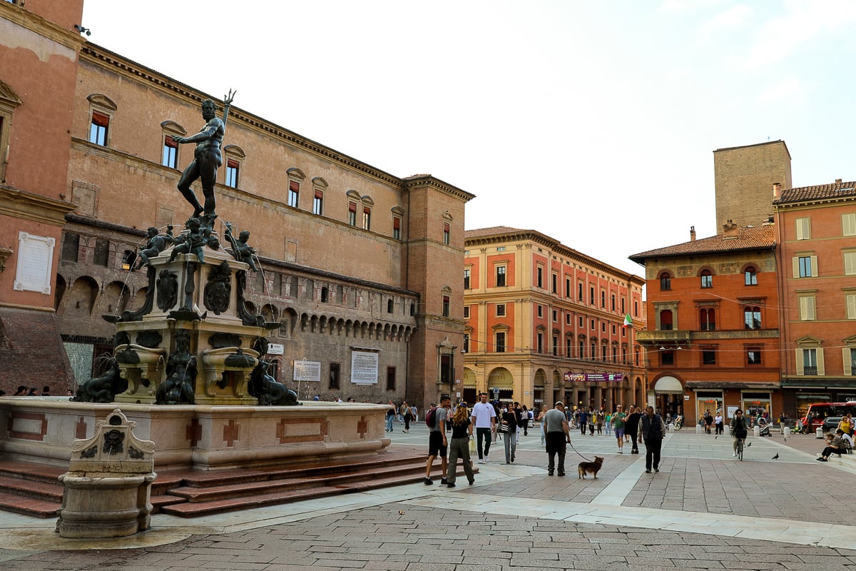 A marble and bronze fountain inside of a bustling square in Bologna, Italy