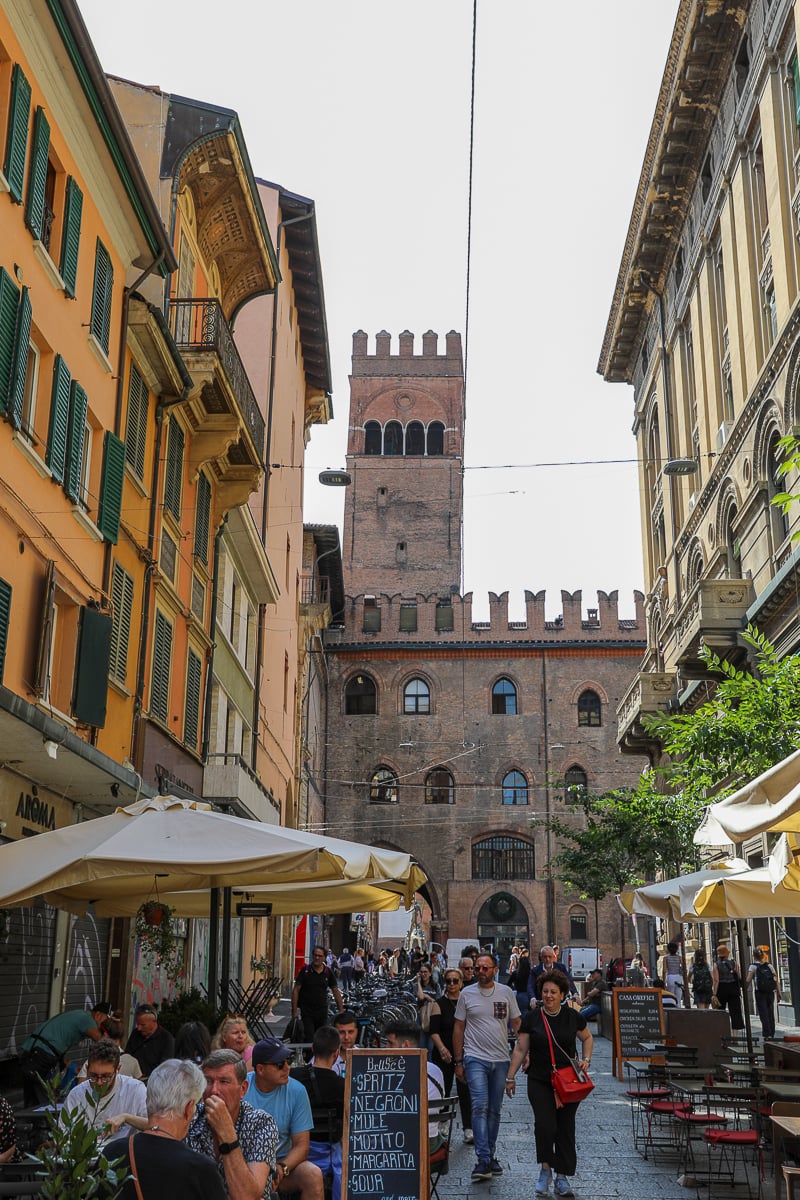 People walking around and sitting at restaurant tables outdoors in the Quadrilatero neighborhood - exploring this area is one of the best things to do in Bologna