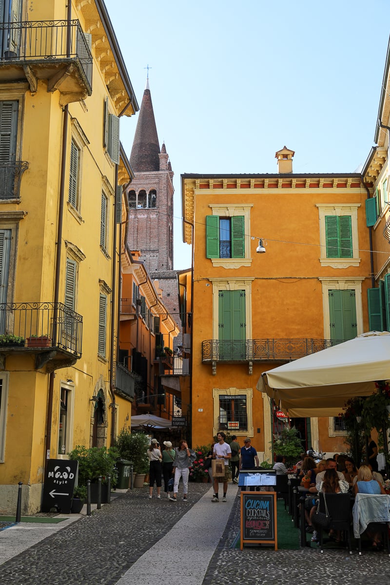 Tall tower behind a crowded restaurant in Verona. Your 2 days in Verona must include can't-miss restaurants along the way!