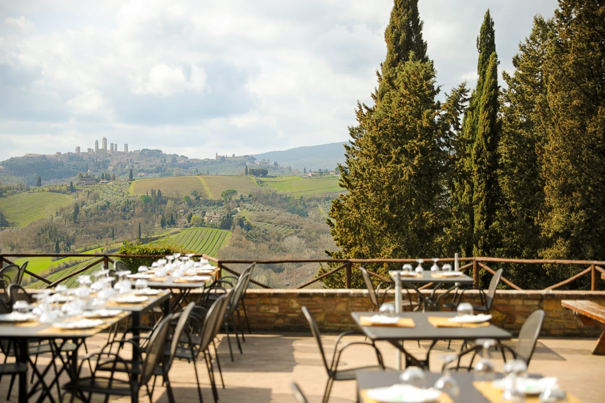 An outdoor dining set-up on a terrace with the hills of Chianti and the town of San Gimignano in the distance