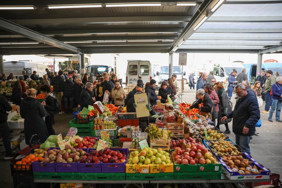An outdoor market with a colorful fruit stall and dozens of people