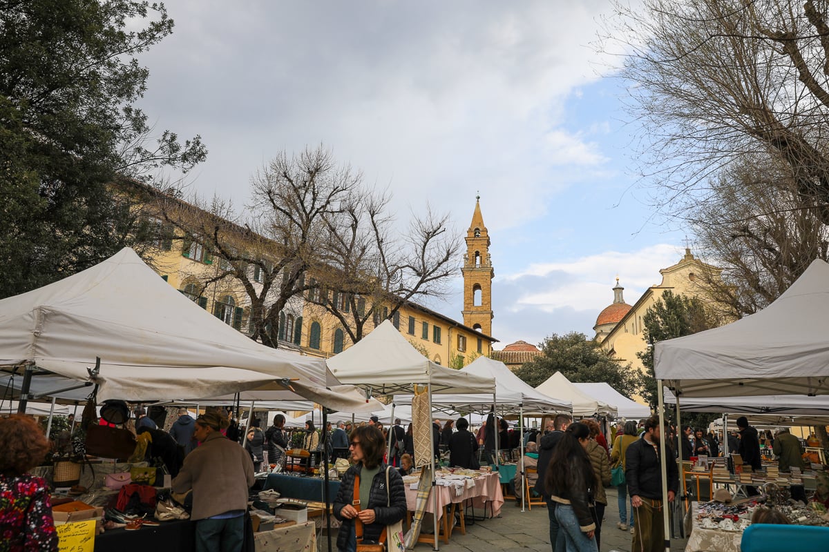 A bustling flea market filled with tented stalls in Piazza Santo Spirito in Florence