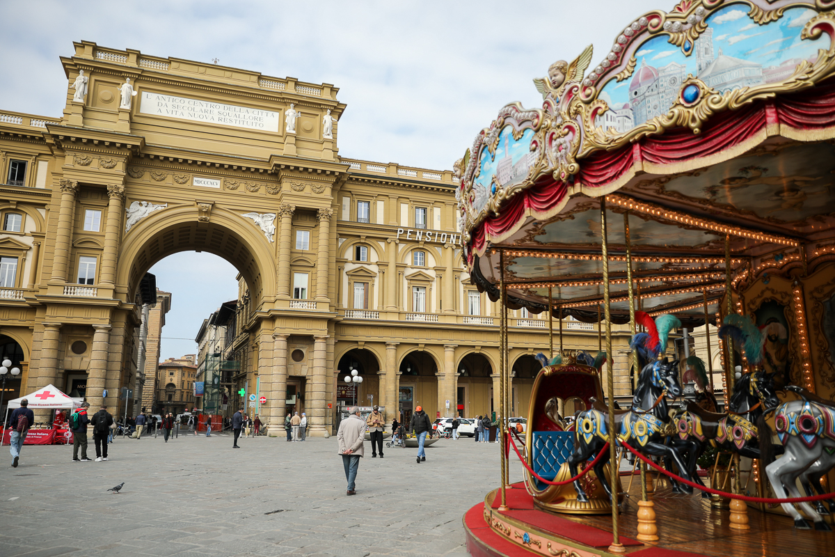 A view of Piazza della Repubblica in Florence with the merry-go-round in the foreground and people walking around under the portico