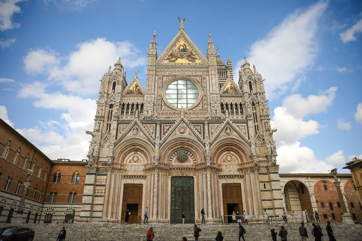 The facade of the Duomo di Siena on a sunny day with people on the steps of the cathedral