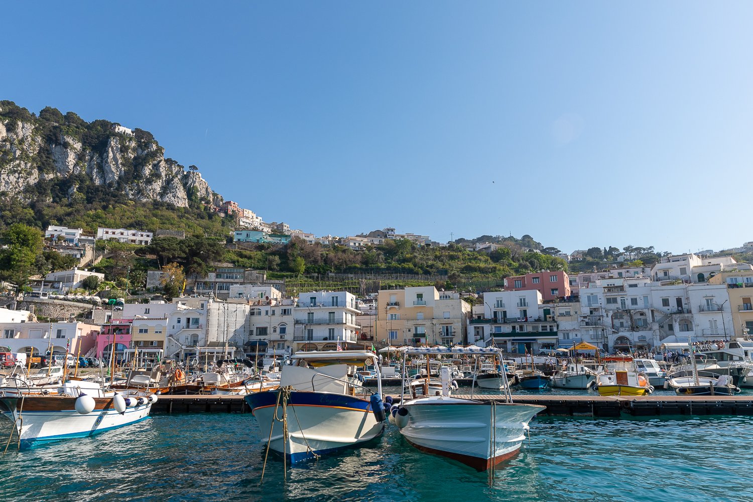 Boats docked by the pier, with rows of colorful buildings on the background on a sunny day in Capri
