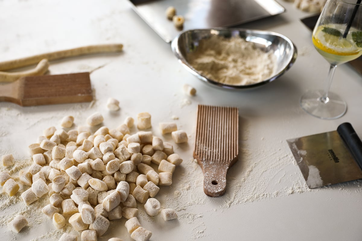 A white table covered in handmade gnocchi, flour, and pasta-making tools