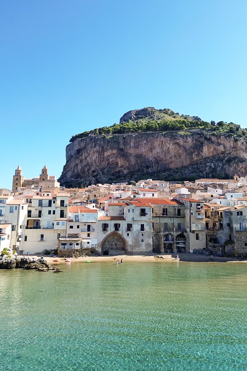 Medieval buildings of Cefalu along the emerald coast with a high cliff behind