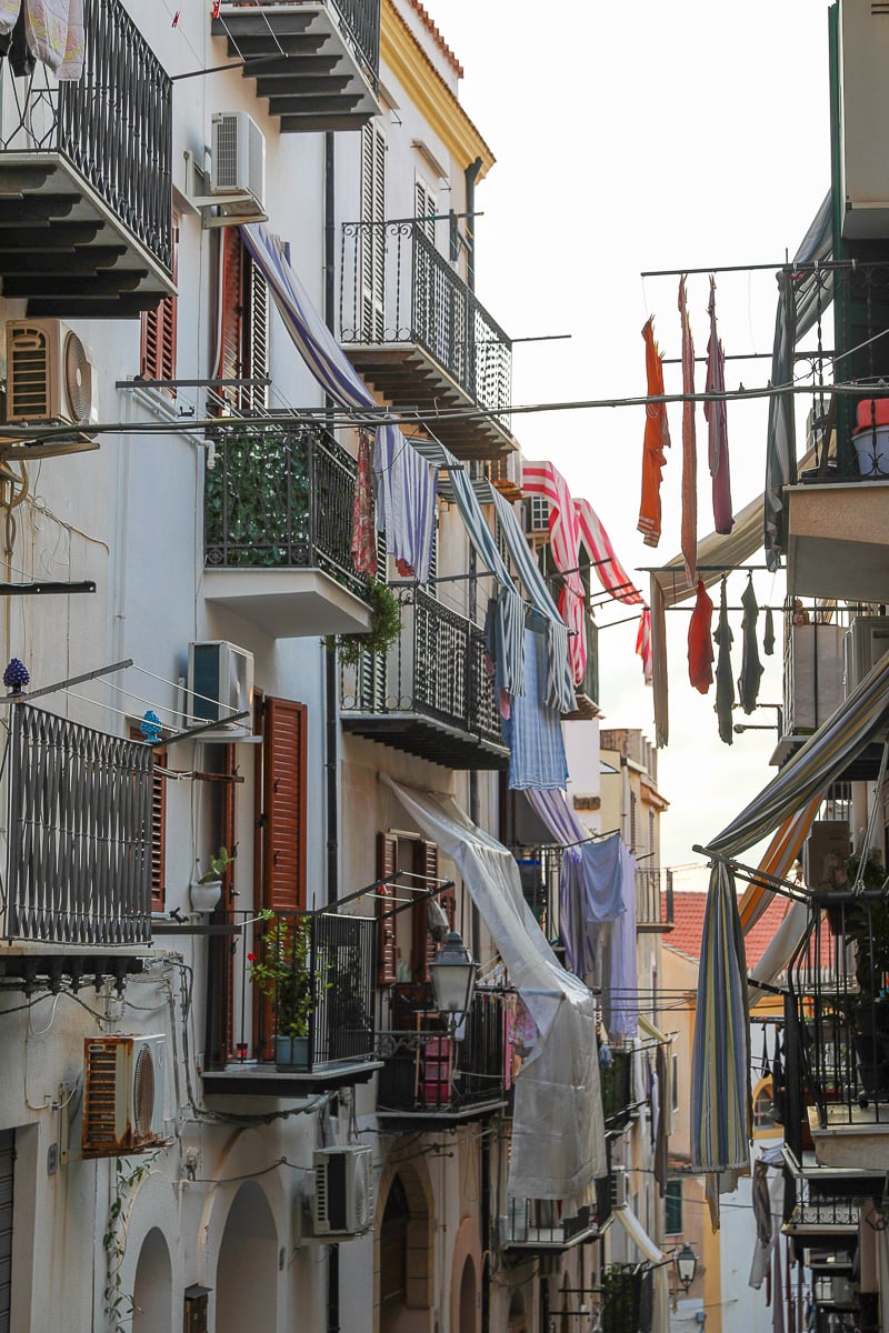Quiet alleyway in Cefalu with apartment buildings decorated with laundry hanging from the balconies