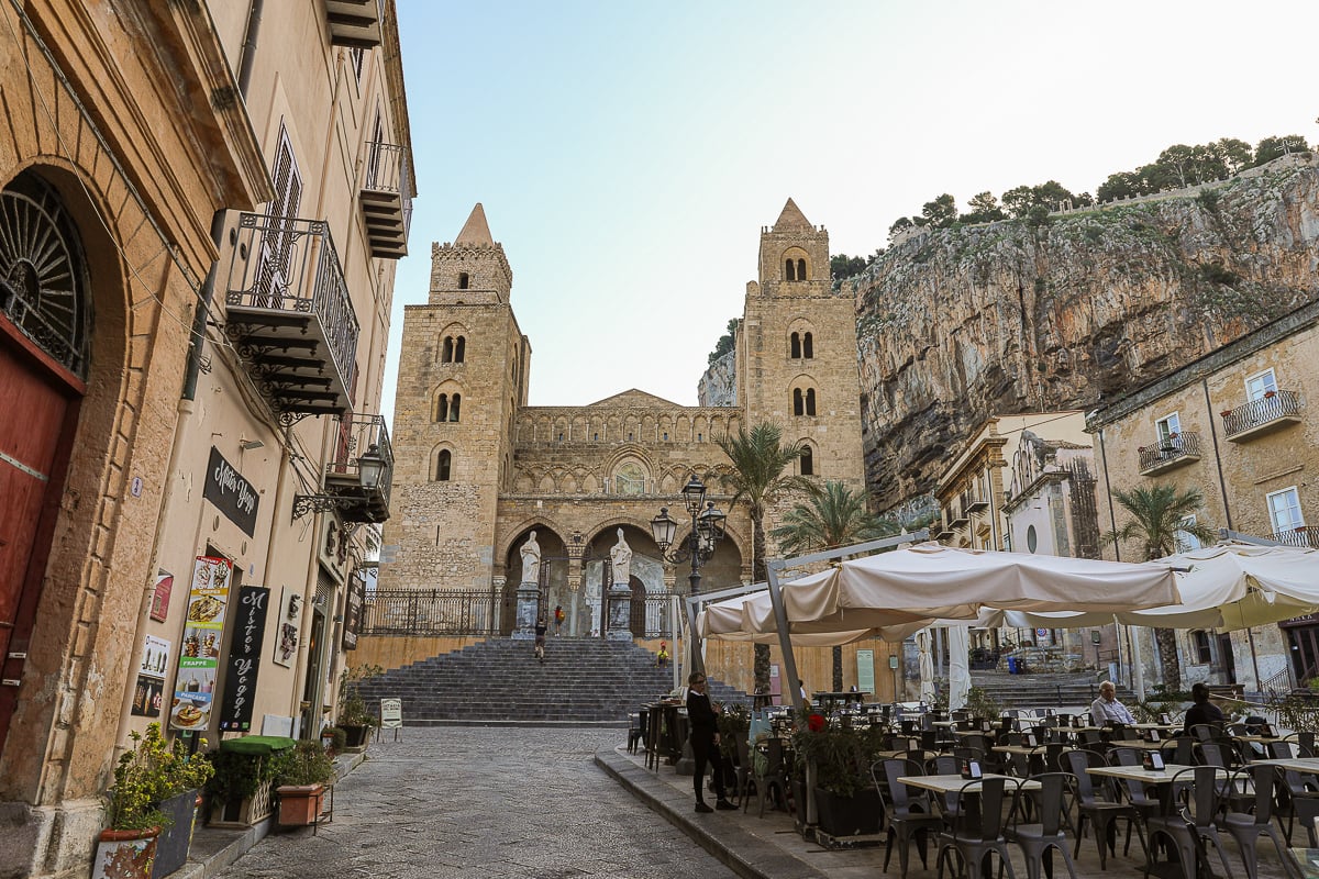 View of Cefalu cathedral in the background and outdoor restaurant tables in the foreground