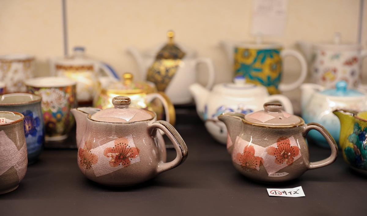 Display of hand-painted Japanese teapots and cups featuring cherry blossom motifs at a Kanazawa lacquerware and pottery shop.