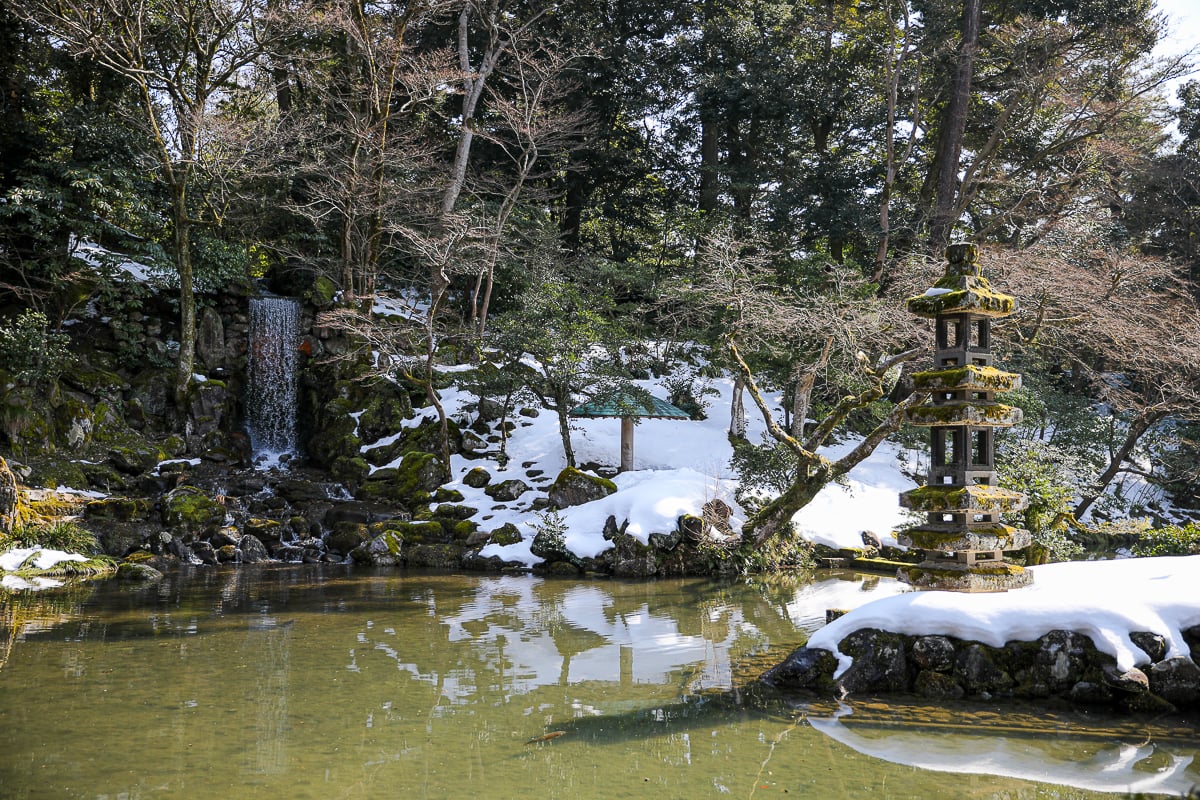 Snow-dusted pond, mossy pagoda lantern, and small waterfall in Kenrokuen Garden, Kanazawa’s most famous landscape garden.