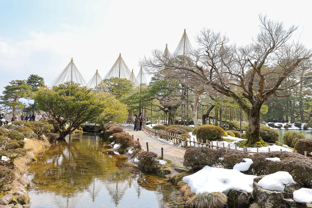 Winter view of Kenrokuen Garden with yukizuri ropes, trees, and ponds covered in snow.