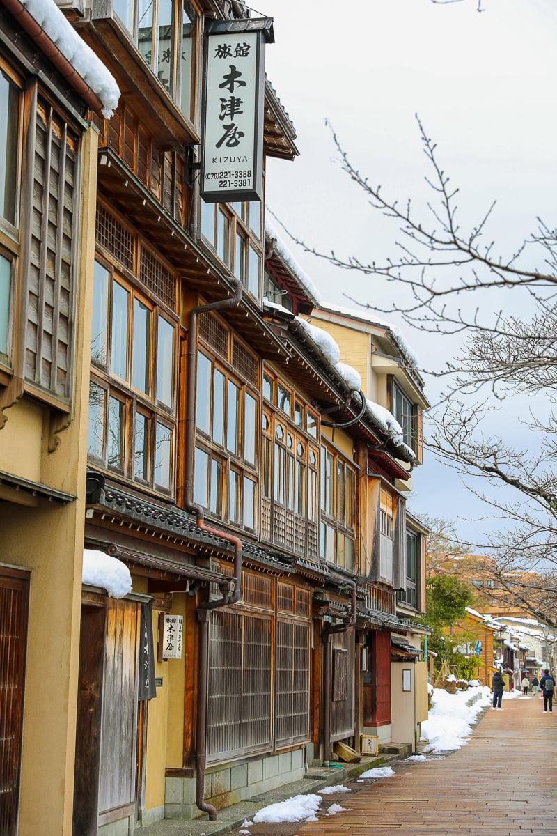 Winter street view in Kanazawa lined with traditional wooden machiya townhouses and snowy rooftops.