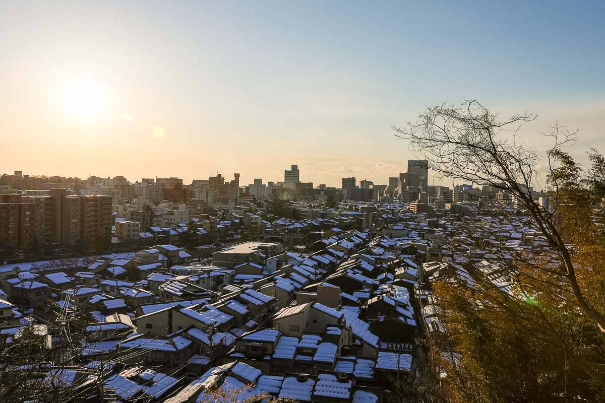 Panoramic winter view over Kanazawa’s rooftops covered in snow, seen from Hosenji Temple at sunset.