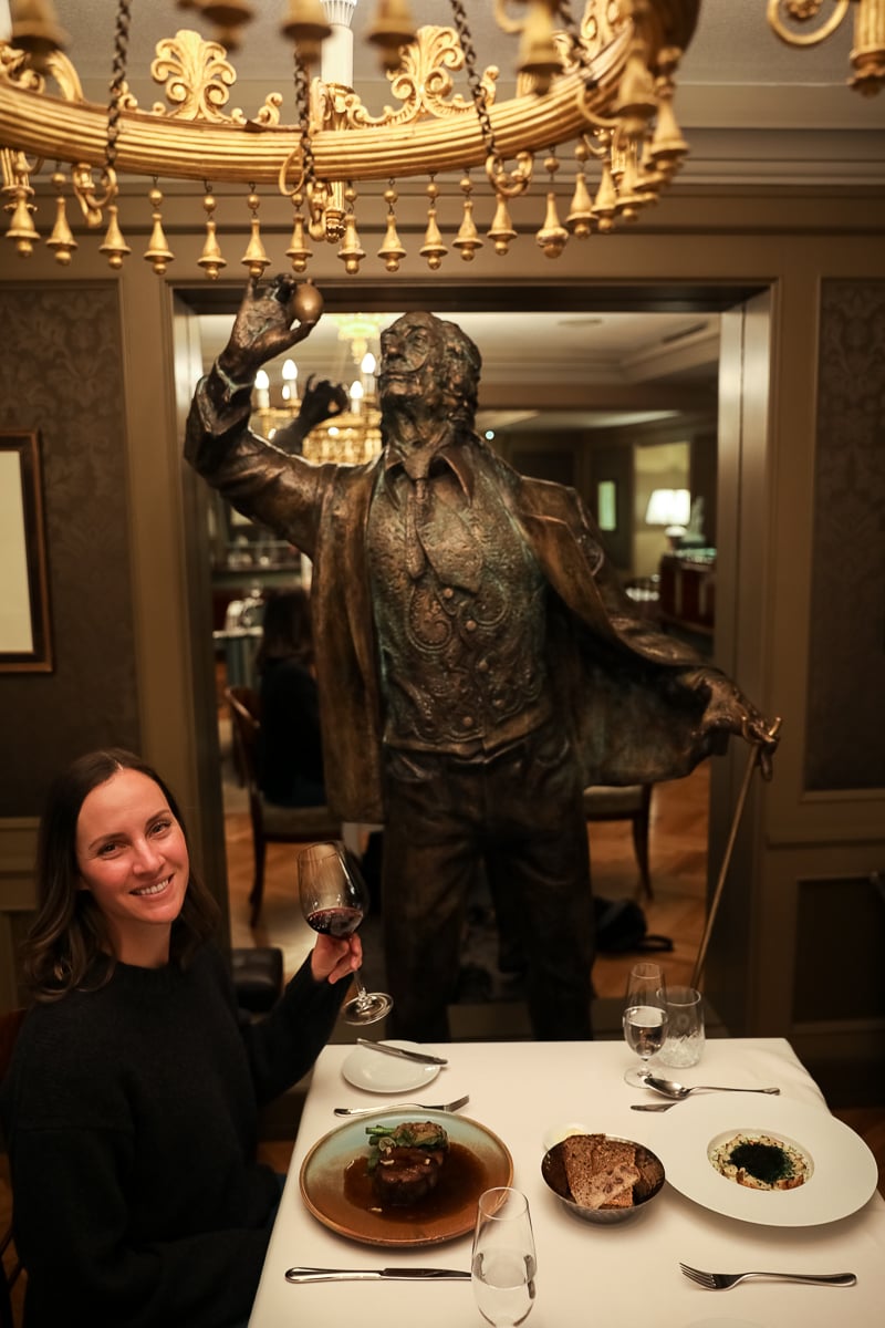 Maddy enjoying her fine-dining main course served at CODA restaurant at the Aria Hotel Prague, with a bronze sculpture in the background
