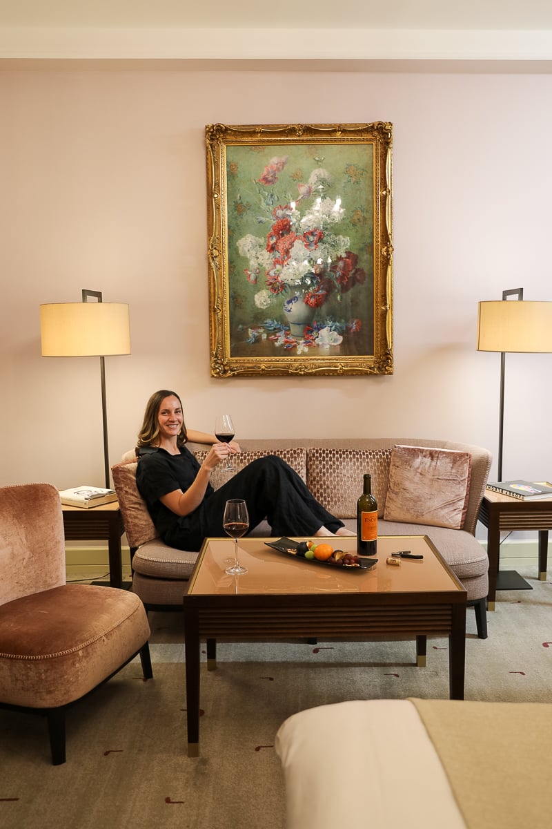 Maddy relaxing with a glass of wine in the elegant room at Aria Hotel Prague, surrounded by plush seating and classical artwork