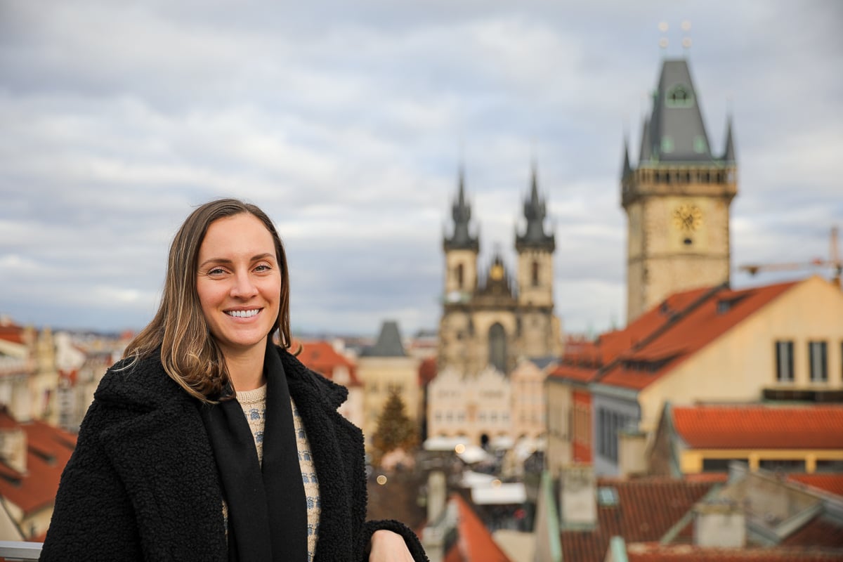 Maddy smiling on Hotel Rott's rooftop terrace with sweeping views of Old Town, including the Church of Our Lady before Týn in the background