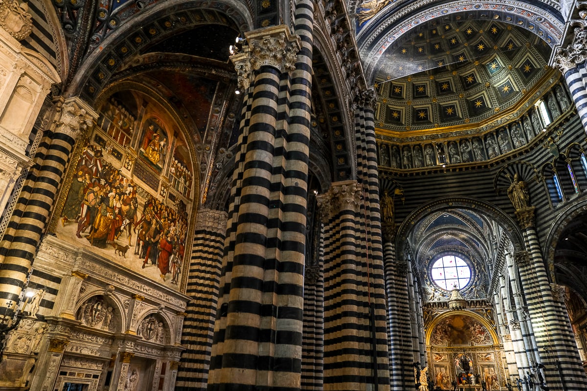 Interior of the Duomo di Siena with black and white marble columns and frescoed ceilings