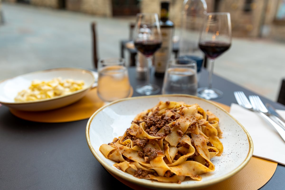 Plate of pappardelle pasta with meat ragù and red wine at an outdoor restaurant in Siena