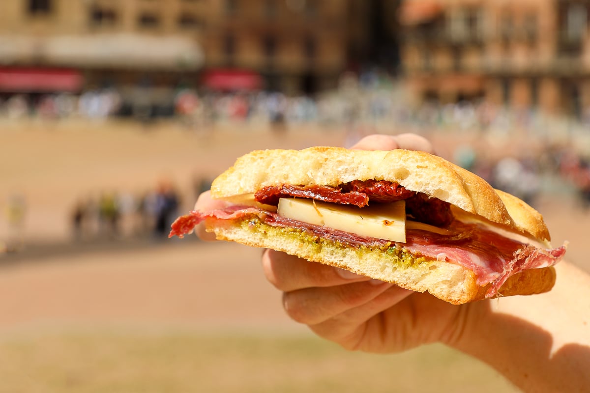 Traditional Tuscan sandwich with cured meat and cheese held over Piazza del Campo in Siena