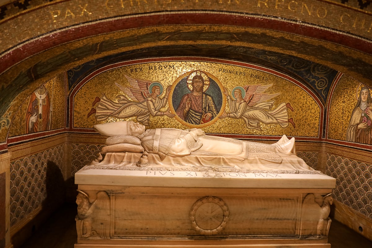 Marble tomb beneath St. Peter’s Basilica with a reclining papal effigy set against a gold mosaic background