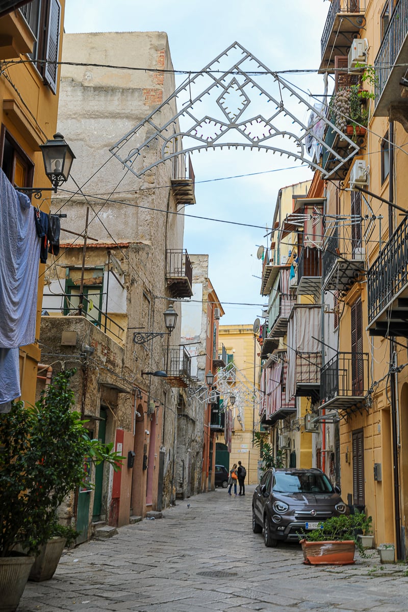 Narrow Palermo alley with colorful balconies, laundry lines, and overhead street lights in Sicily