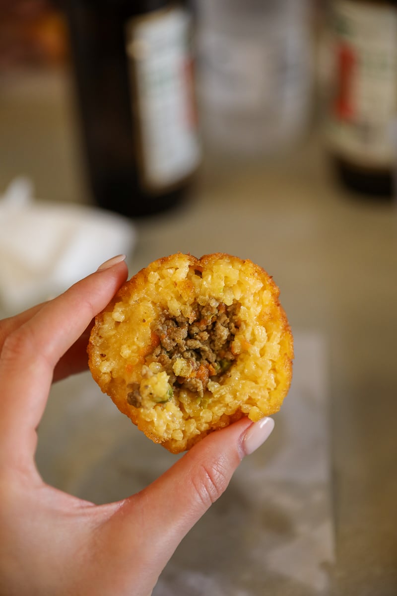 Half-eaten arancina with ragù filling held in hand, classic Palermo street food in Sicily