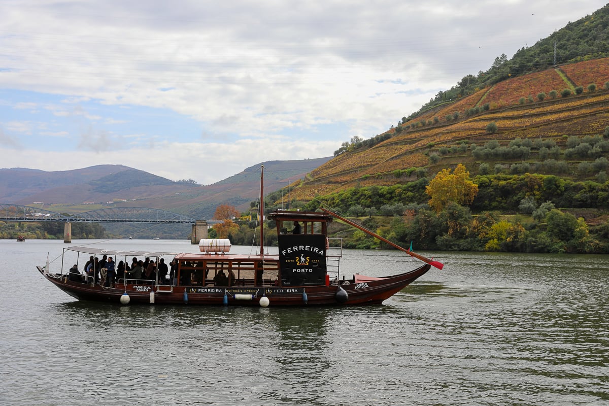 Traditional rabelo boat cruising the Douro River past terraced vineyards in Portugal’s Douro Valley