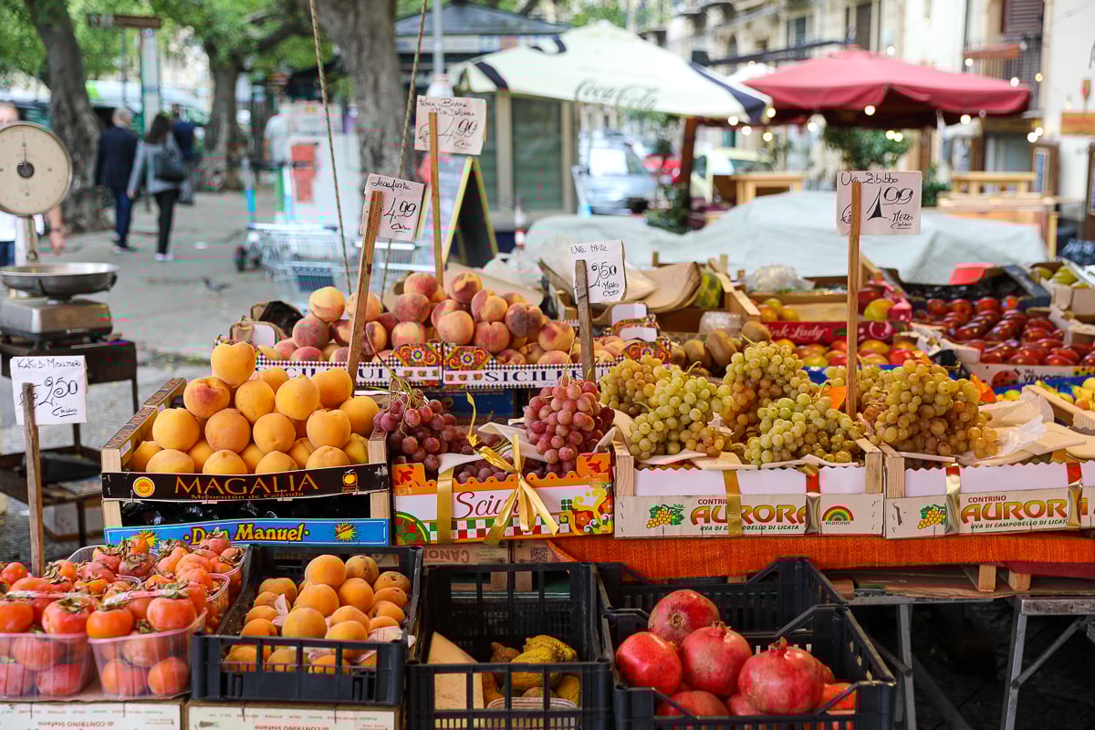 Colorful fruit stand at a Palermo street market with peaches, grapes, apricots, and handwritten price signs in Sicily