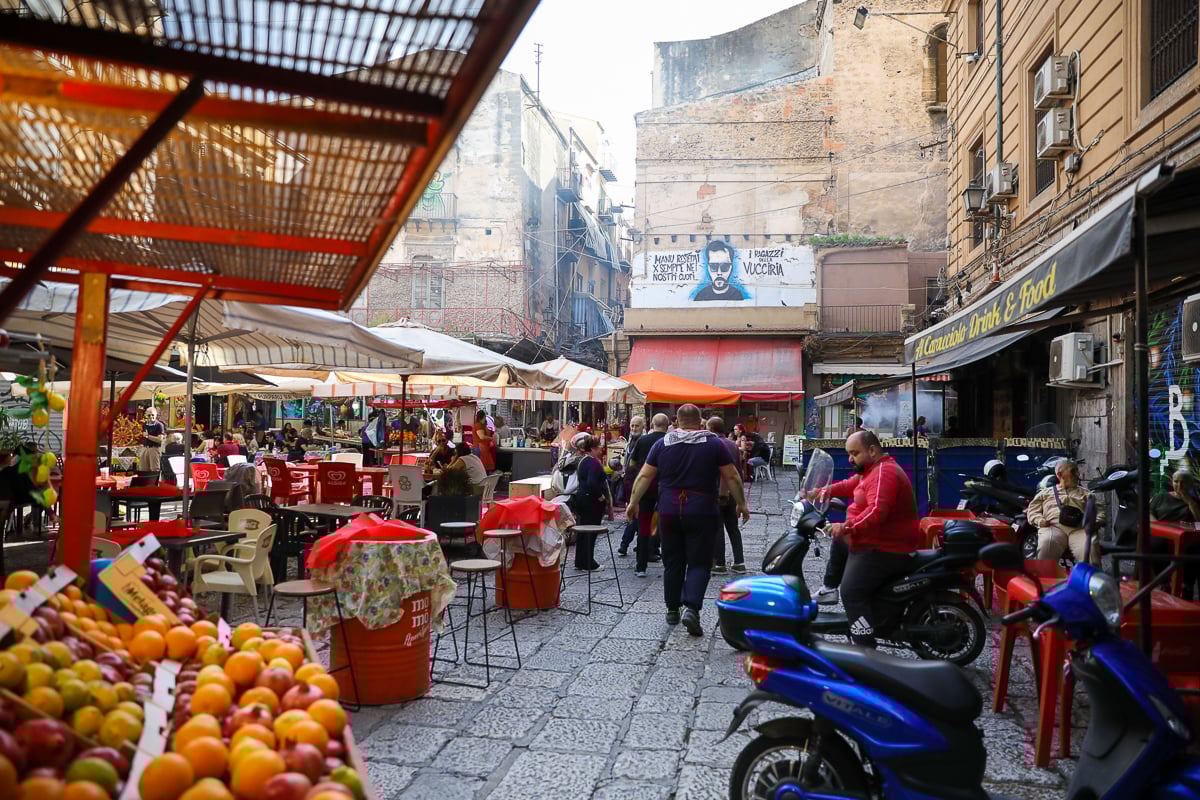 La Vucciria Market in Palermo with street food stalls, scooters, and outdoor tables in Sicily