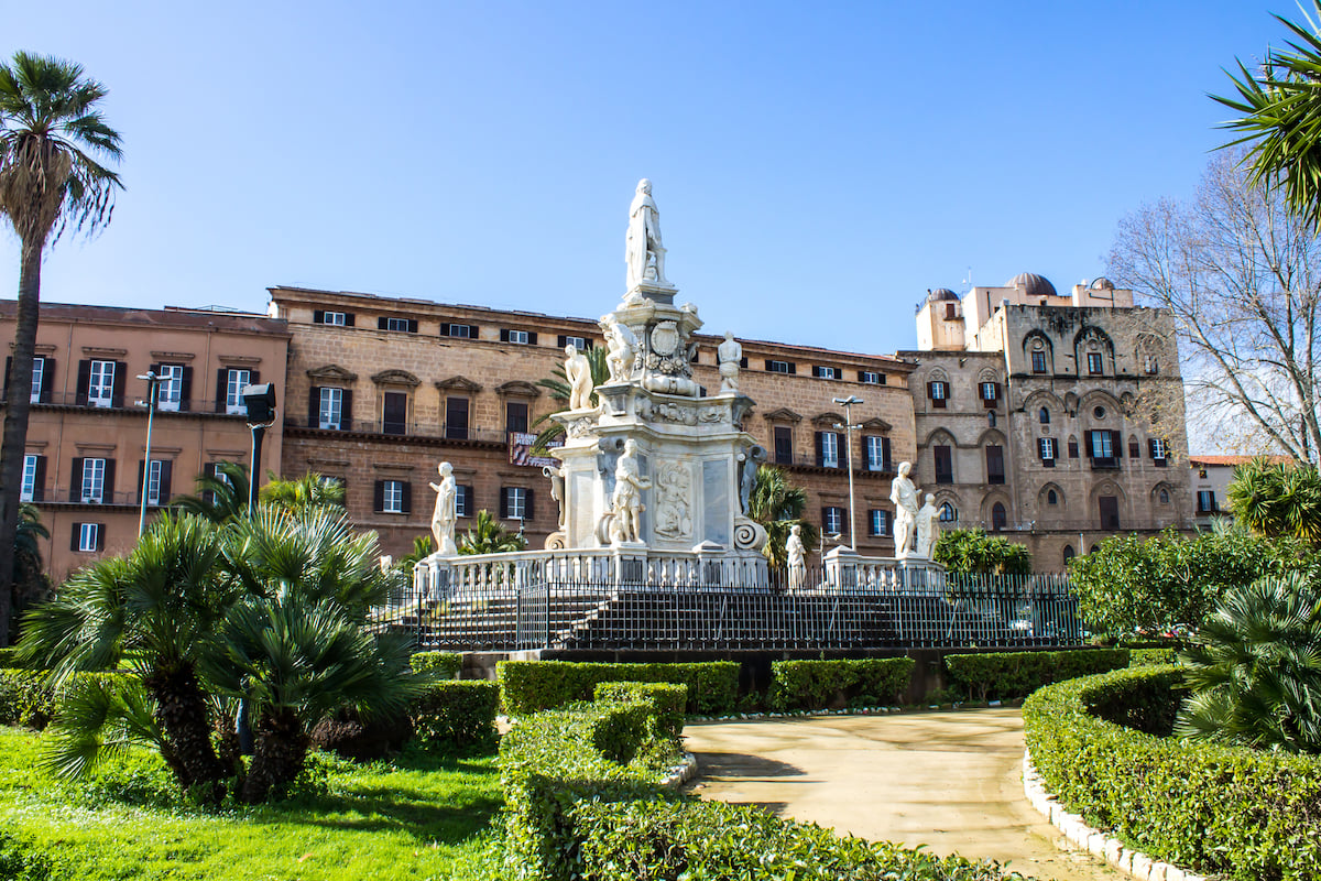 Palazzo dei Normanni exterior in Palermo with formal gardens and a white monument in the foreground