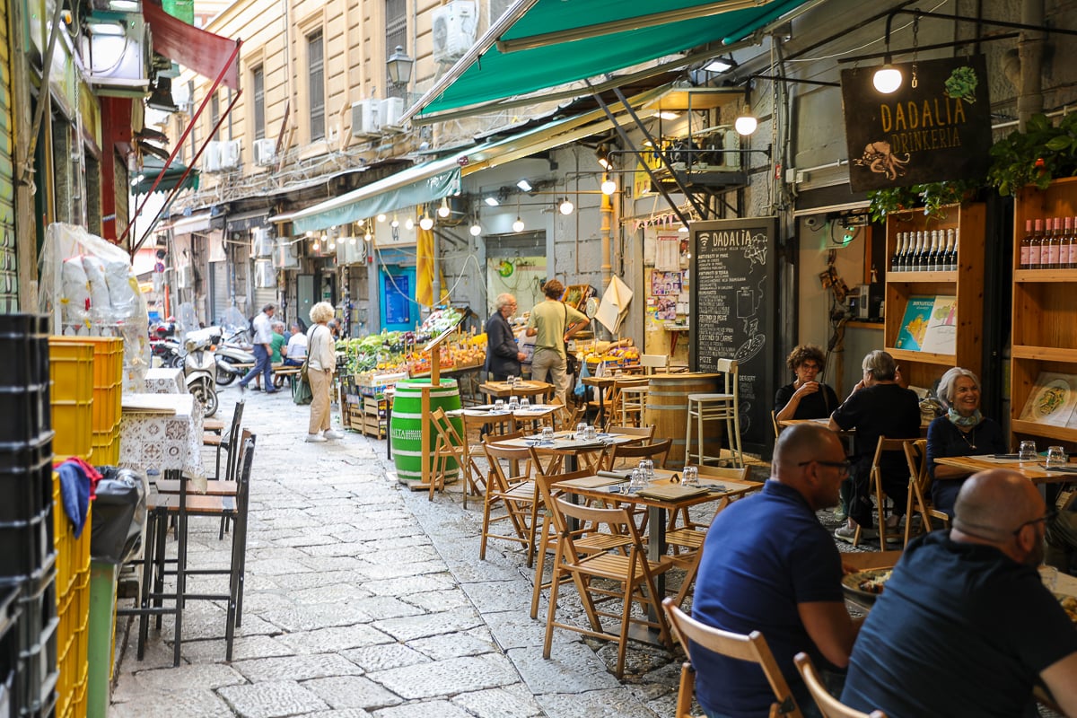 Outdoor dining scene on a Palermo market street with café tables, string lights, and locals eating in Sicily