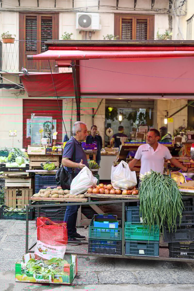 Palermo market scene with local vendors and fresh produce stands under colorful awnings in Sicily