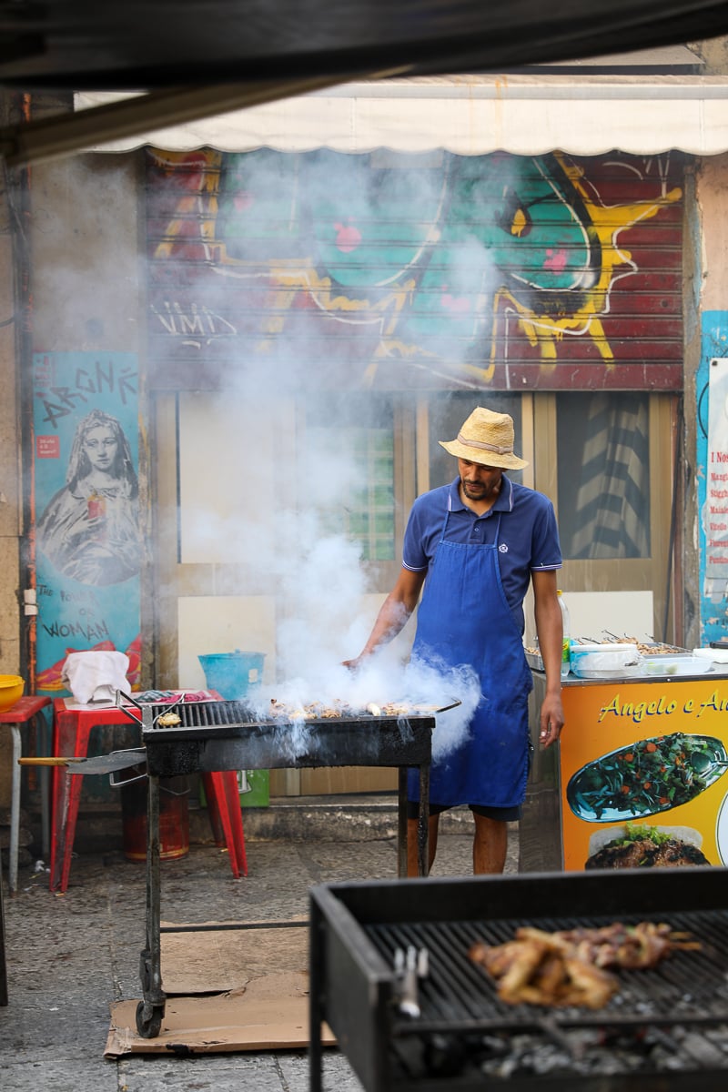 Street grill cooking meat skewers with smoke rising at a Palermo market stall in Sicily