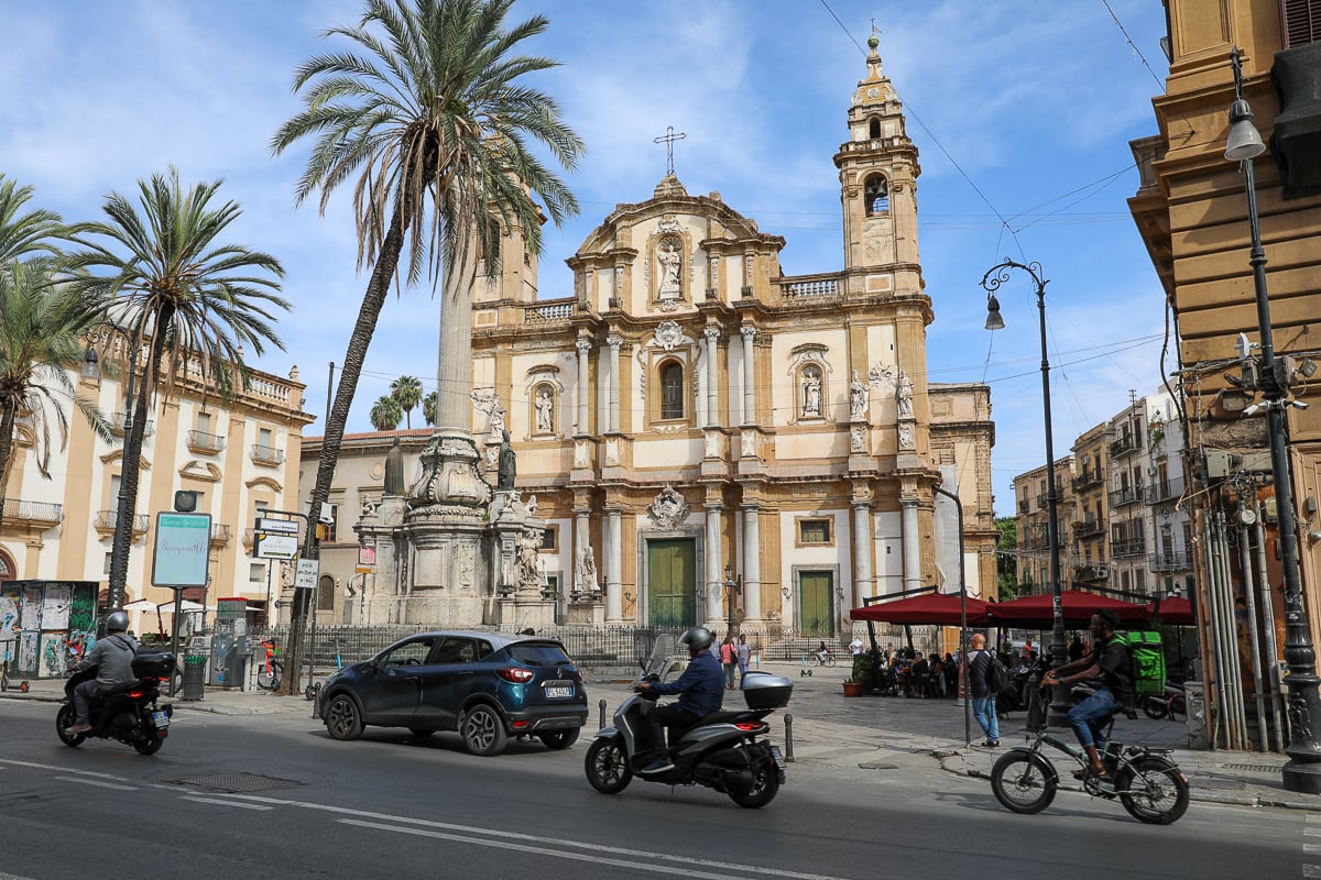 Palermo piazza with a baroque church, palm trees, scooters, and outdoor cafés in Sicily