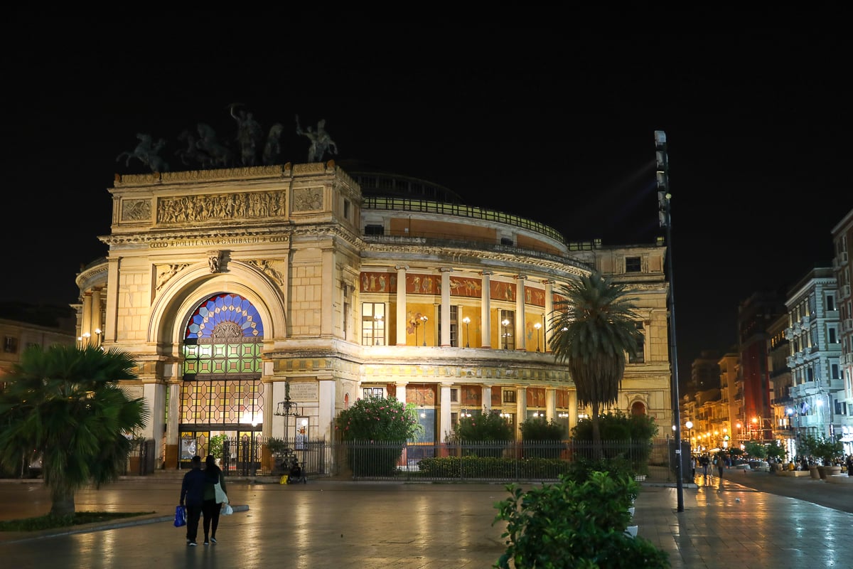 Night view of Teatro Politeama Garibaldi lit up, with palm trees and the piazza