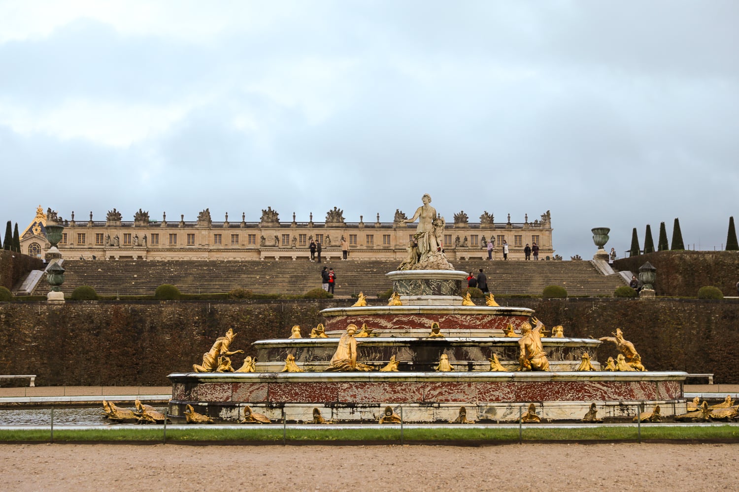 Fountain in the Gardens of Versailles with gilded statues and the palace terraces in the distance