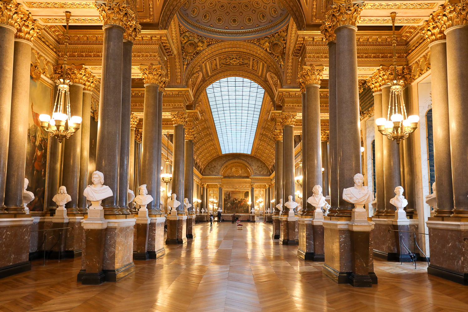 Gallery of Battles at Versailles Palace with gilded columns, marble floors, and busts lining the hall