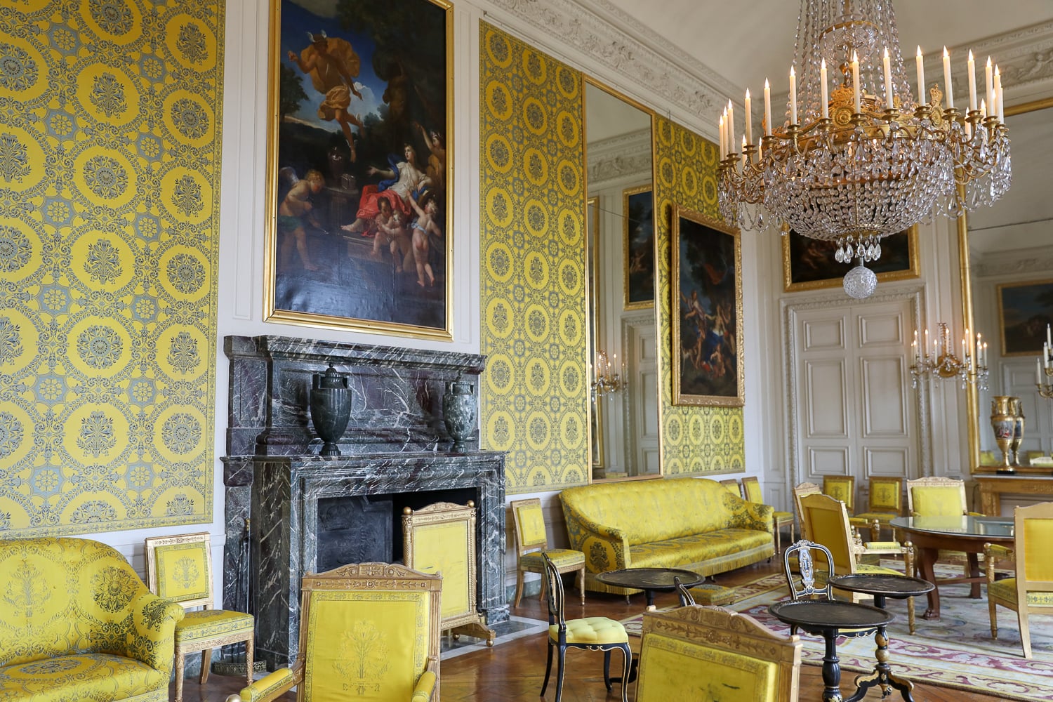 Grand Trianon salon at Versailles with yellow damask walls, marble fireplace, and crystal chandelier