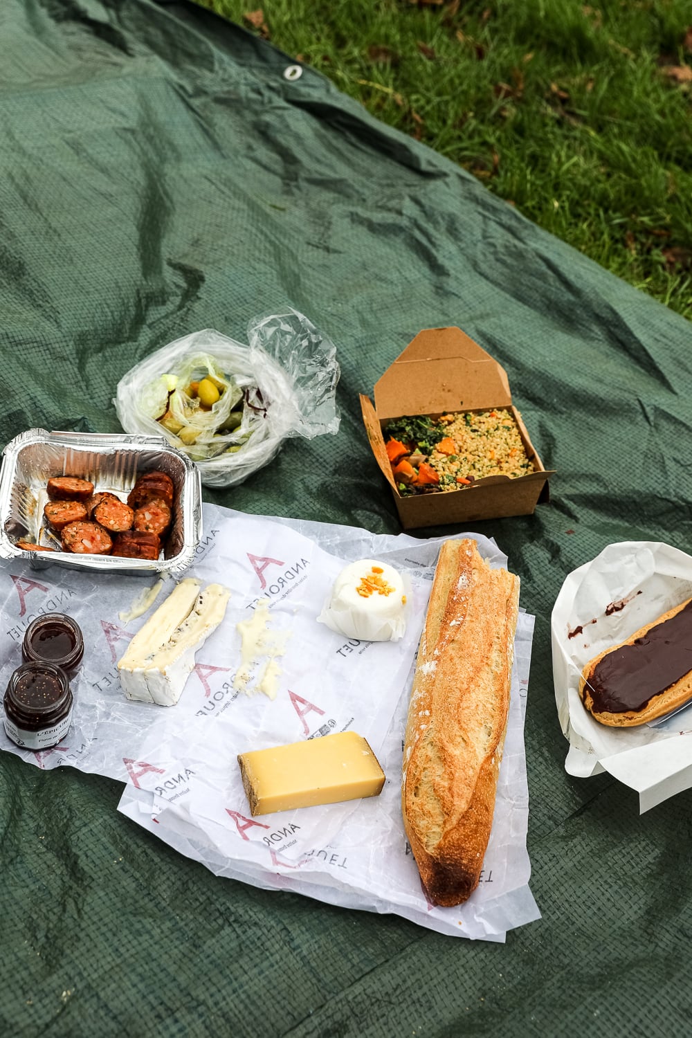 Picnic lunch on the Versailles palace grounds with baguette, cheeses, sausages, olives, and a chocolate éclair
