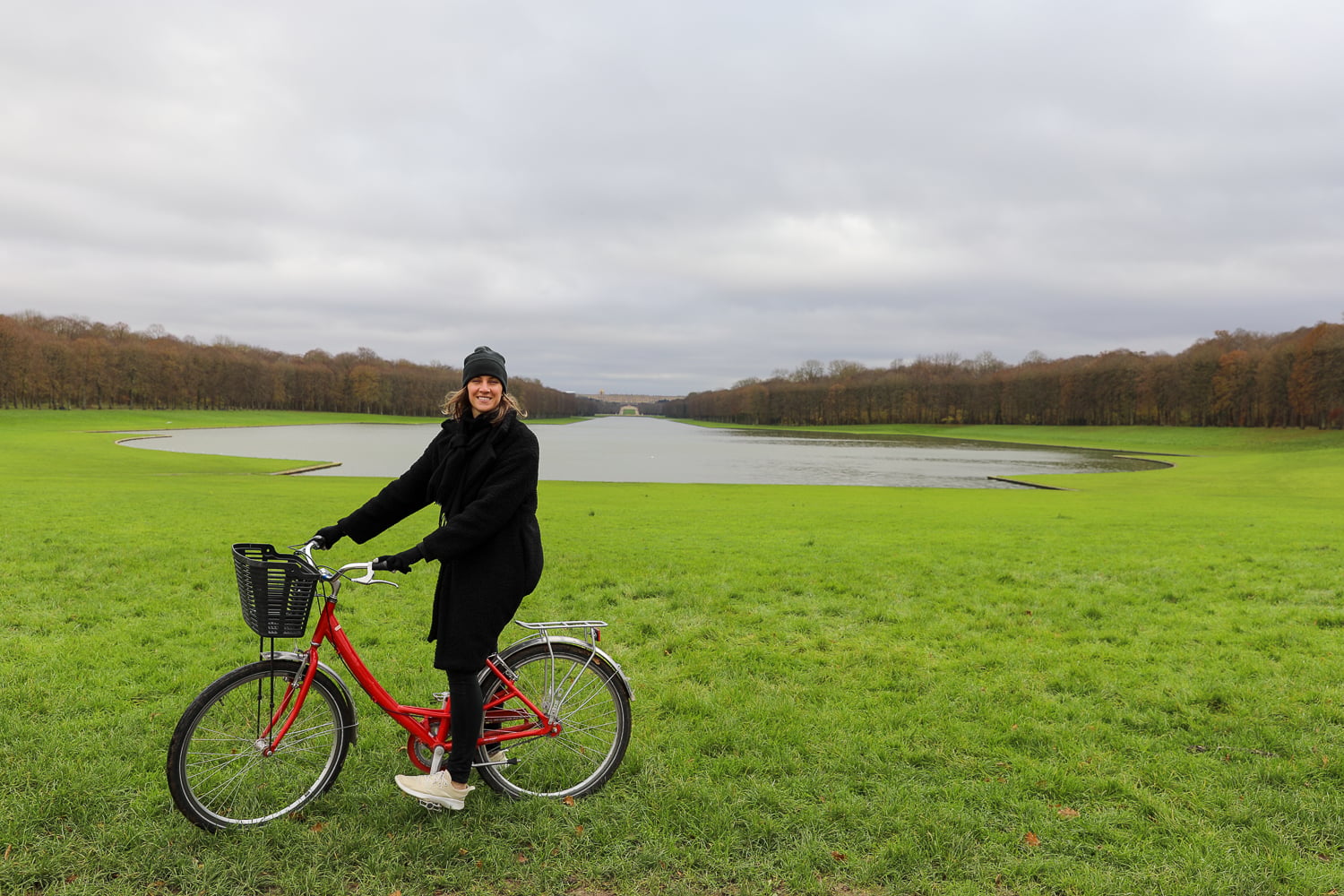 Traveler on a red bicycle near the Grand Canal at Versailles with wide lawns and cloudy sky