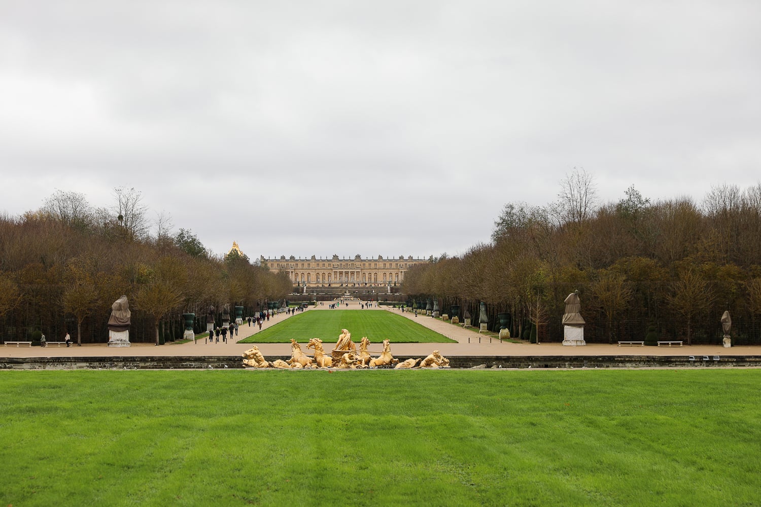 View across the Versailles gardens toward the palace with golden fountain sculptures in the foreground