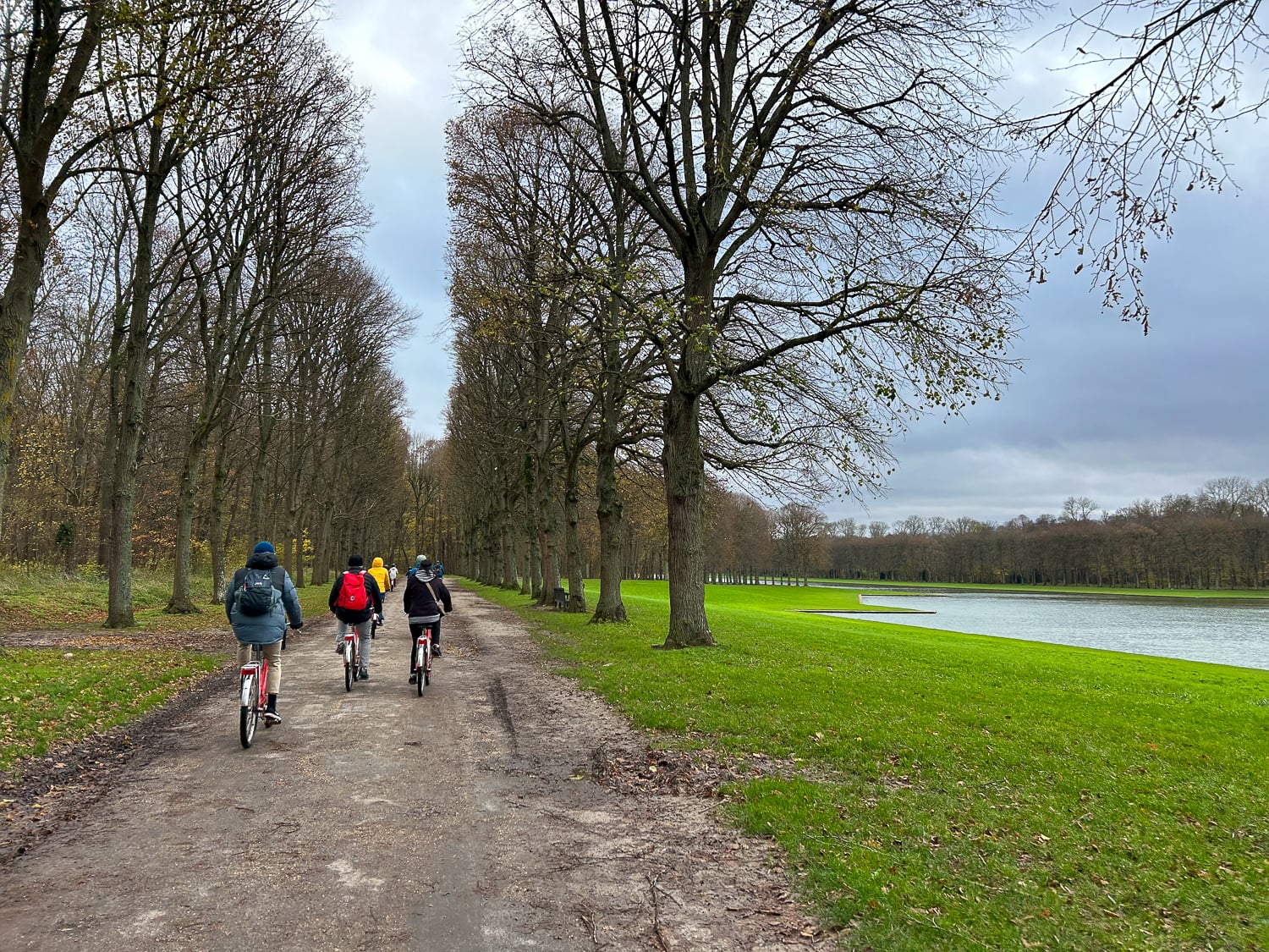 Small group on a Versailles day trip from Paris biking along a tree-lined path beside the Grand Canal on the Versailles estate