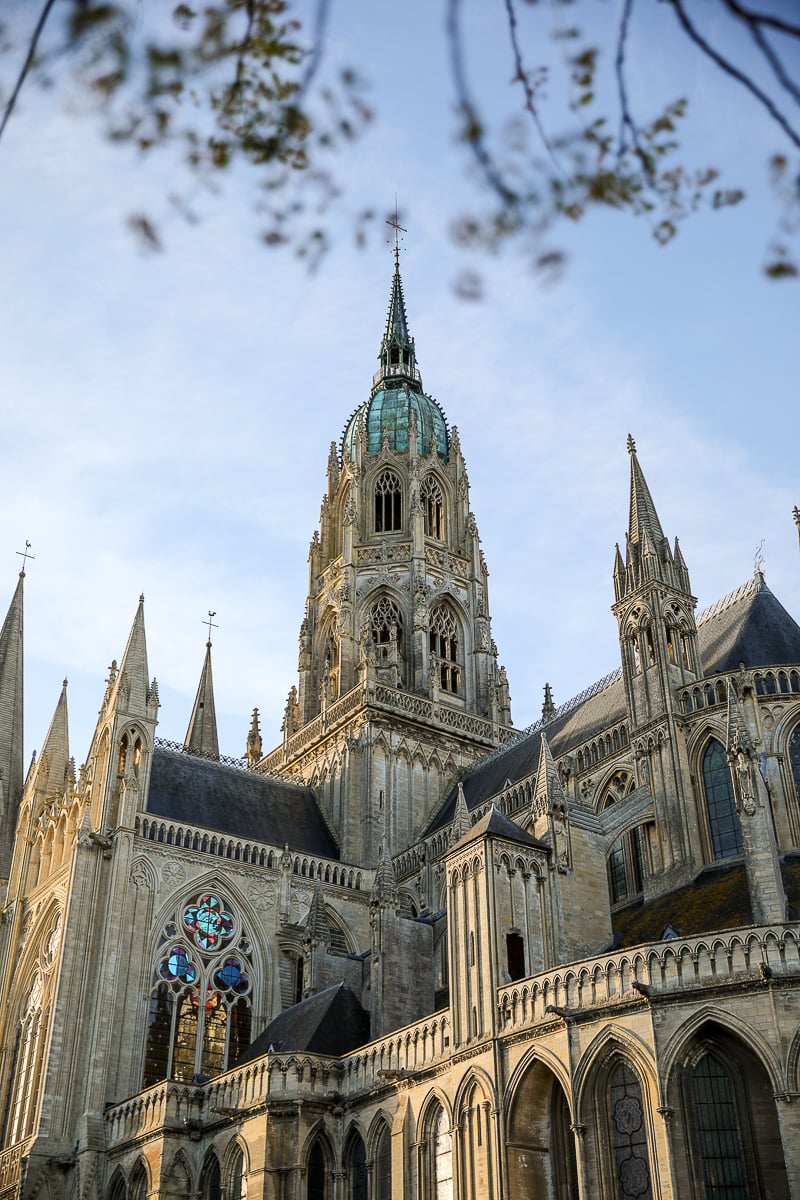 Gothic tower and flying buttresses of Bayeux Cathedral framed by spring tree branches