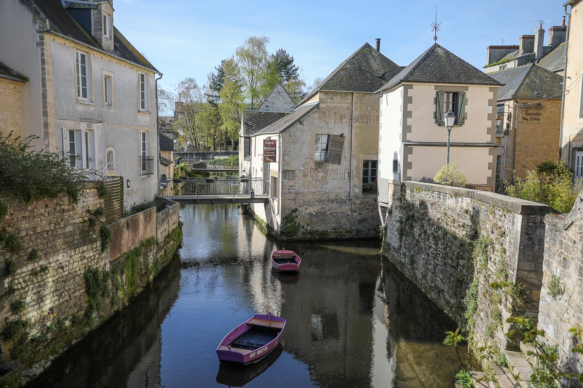 Two small boats moored on the Aure River beside stone buildings in the old town of Bayeux