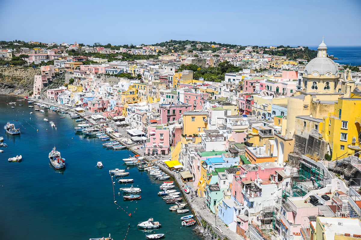 Aerial view of Marina Corricella's colorful houses and yellow church dome above the harbor in Procida, Italy