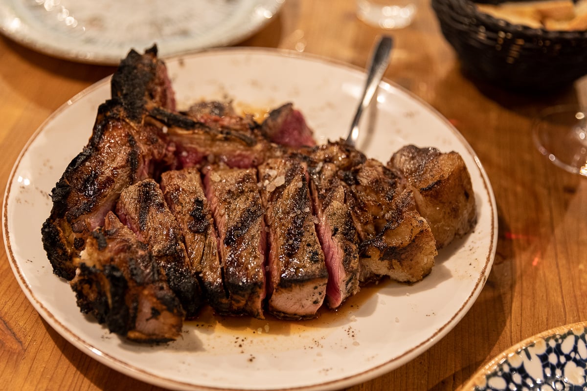 Sliced bistecca alla Fiorentina, a thick rare T-bone Florentine steak, served on a white plate in Florence.